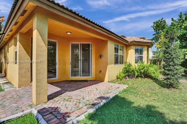 back of house with a yard, stucco siding, a tiled roof, and a patio area
