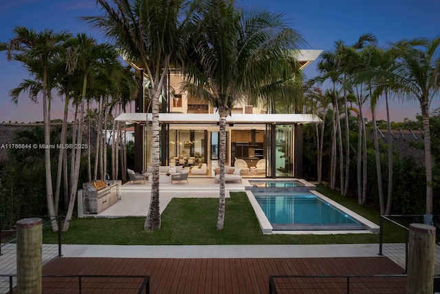 pool at dusk featuring a patio, an outdoor living space, a yard, and a pool with connected hot tub