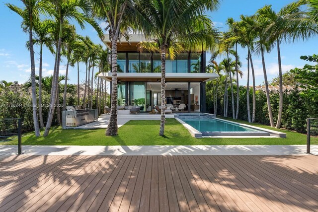 pool with a deck, an outdoor living space, a yard, a ceiling fan, and exterior kitchen