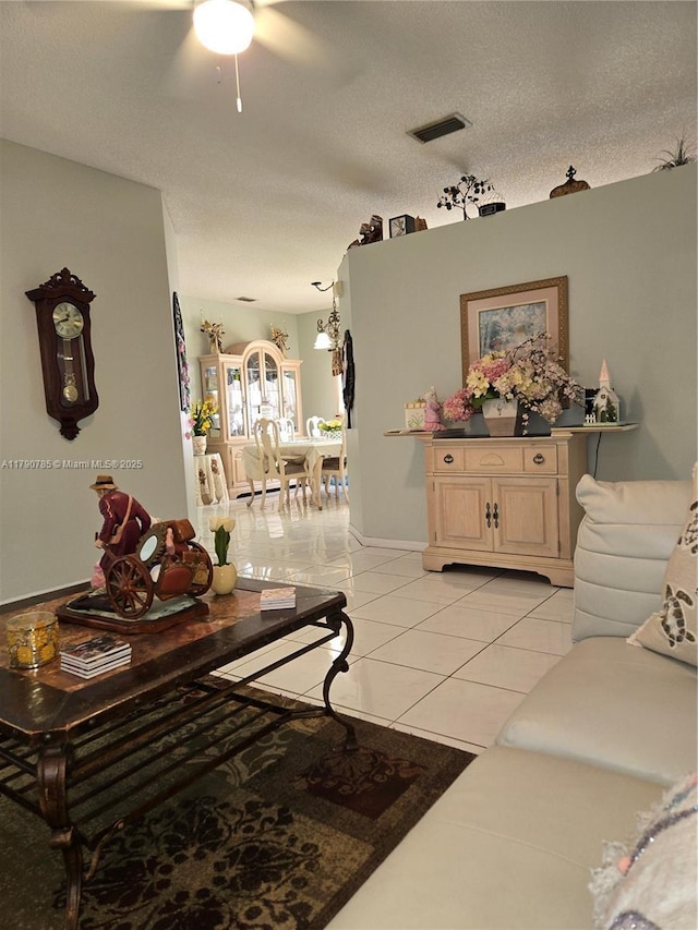 living area featuring light tile patterned floors, visible vents, and ceiling fan