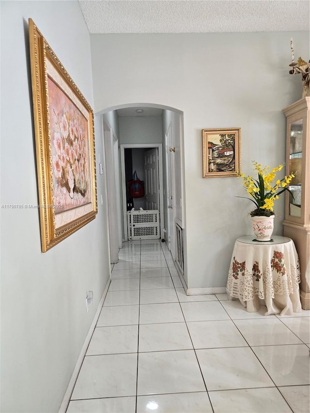 corridor with light tile patterned floors, baseboards, a textured ceiling, and arched walkways