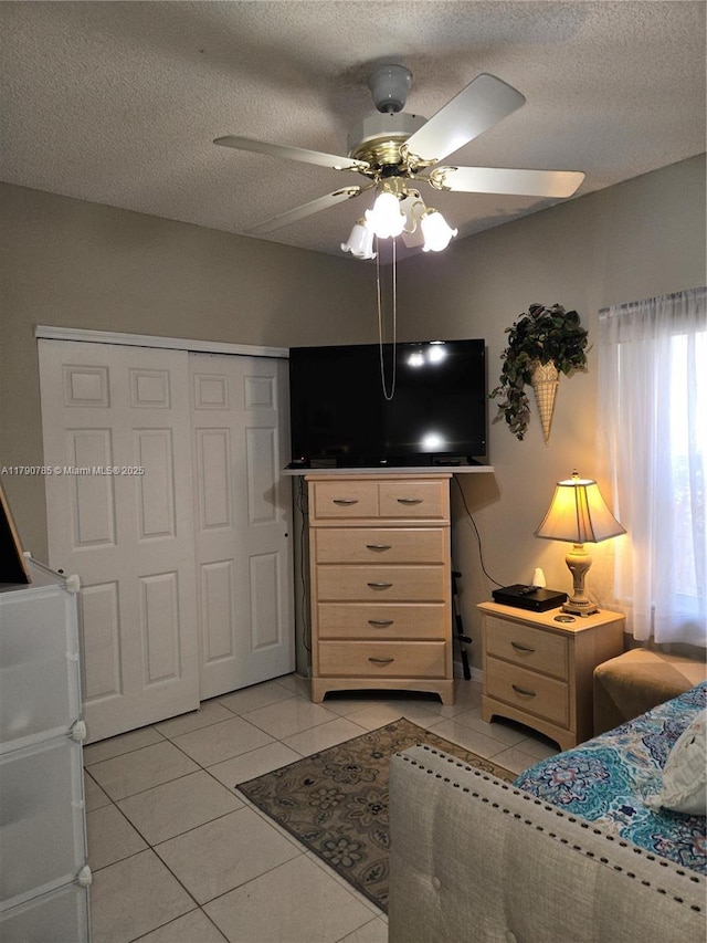 bedroom featuring light tile patterned floors, a closet, ceiling fan, and a textured ceiling