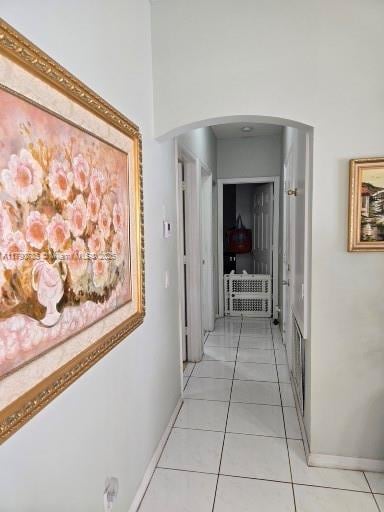hall featuring baseboards, light tile patterned floors, arched walkways, and a high ceiling