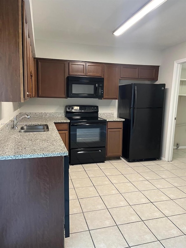 kitchen featuring light stone counters, a sink, dark brown cabinetry, black appliances, and light tile patterned flooring