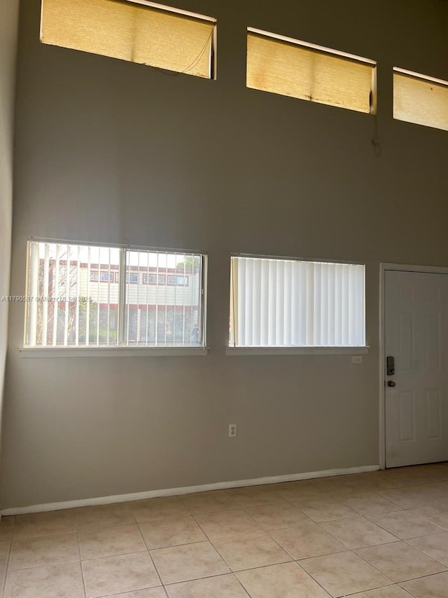 empty room featuring light tile patterned floors, a towering ceiling, and baseboards