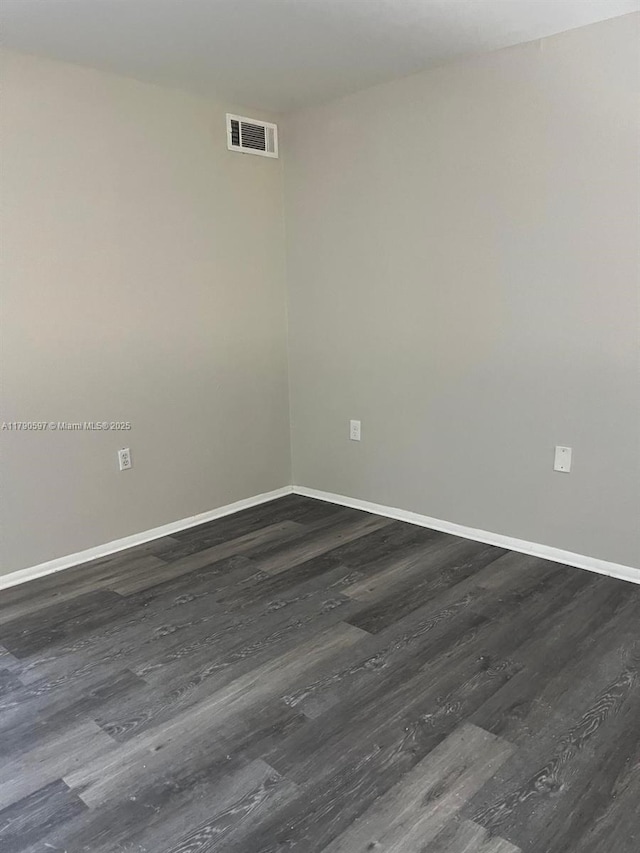empty room with visible vents, dark wood-style floors, and baseboards
