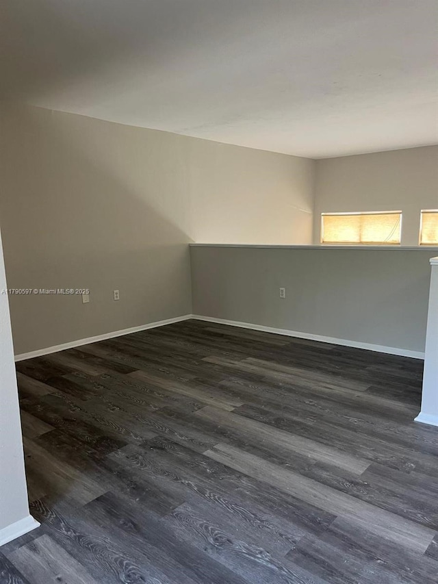 unfurnished room with baseboards and dark wood-type flooring