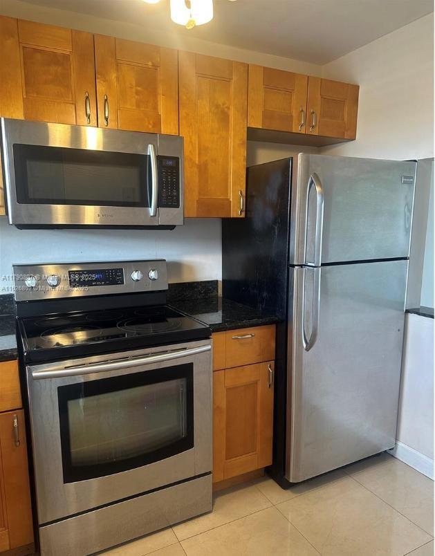8400 Sunrise Lakes Blvd Unit 310, Sunrise, FL 33322 - kitchen featuring appliances with stainless steel finishes, brown cabinetry, light tile patterned flooring, and dark stone countertops