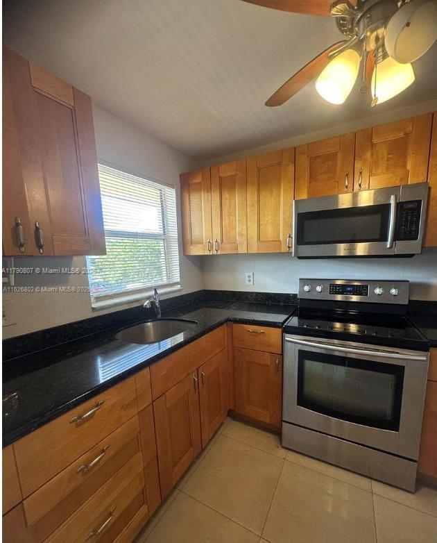 8400 Sunrise Lakes Blvd Unit 310, Sunrise, FL 33322 - kitchen featuring stainless steel appliances, a sink, light tile patterned floors, dark stone counters, and brown cabinetry