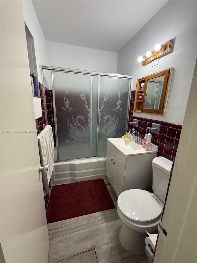 full bath featuring wainscoting, tile walls, enclosed tub / shower combo, toilet, and vanity