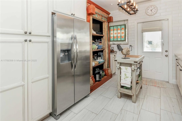 kitchen with an inviting chandelier, light countertops, white cabinets, and stainless steel fridge