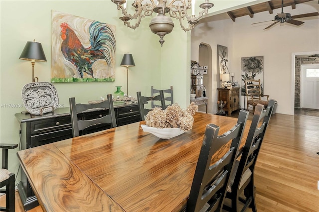dining room with beamed ceiling, arched walkways, wood finished floors, and ceiling fan with notable chandelier
