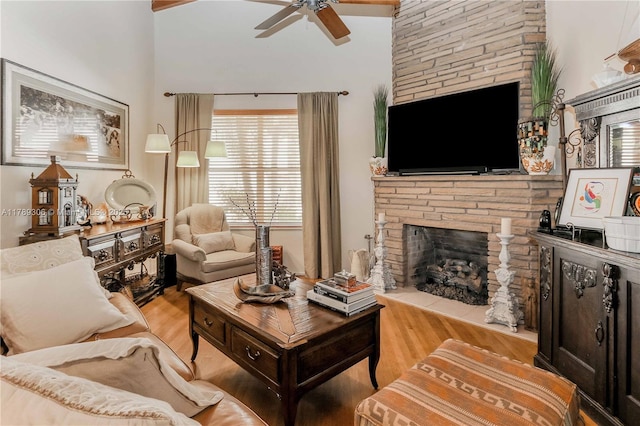 living room with wood finished floors, ceiling fan, and a stone fireplace