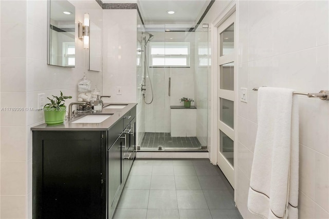 full bath with a sink, a stall shower, tile patterned flooring, and tile walls
