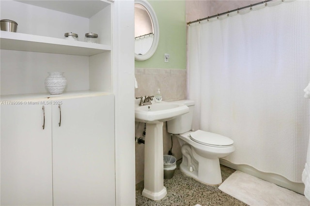 bathroom featuring a shower with curtain, speckled floor, tile walls, toilet, and wainscoting