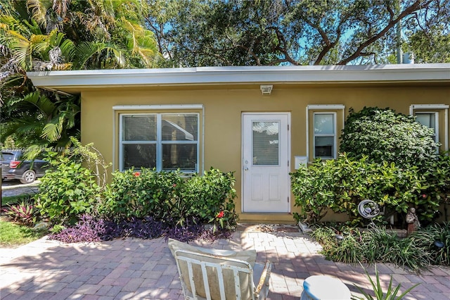 view of exterior entry with stucco siding and a patio area