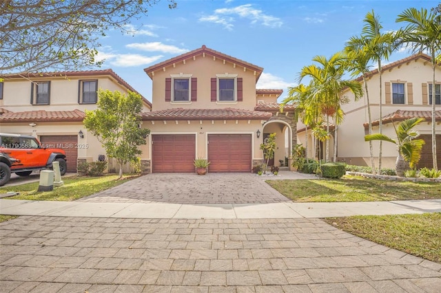 mediterranean / spanish home featuring stucco siding, a tiled roof, decorative driveway, a front yard, and an attached garage