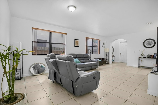 living area featuring visible vents, light tile patterned floors, arched walkways, and baseboards