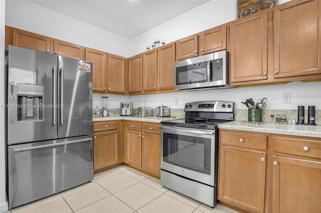 kitchen featuring light tile patterned floors, appliances with stainless steel finishes, and brown cabinets