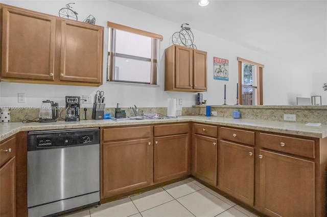 kitchen with light tile patterned floors, brown cabinets, stainless steel dishwasher, a sink, and a peninsula