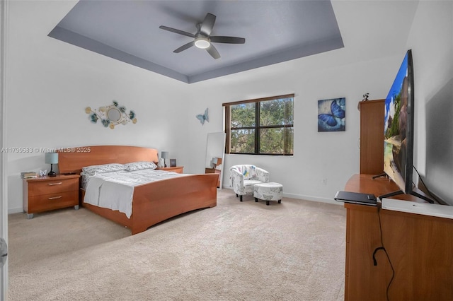bedroom featuring light colored carpet, ceiling fan, a tray ceiling, and baseboards