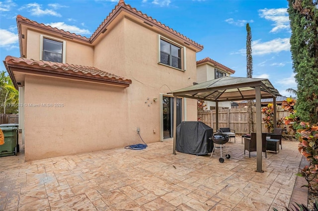 back of property featuring a tile roof, a gazebo, stucco siding, and fence