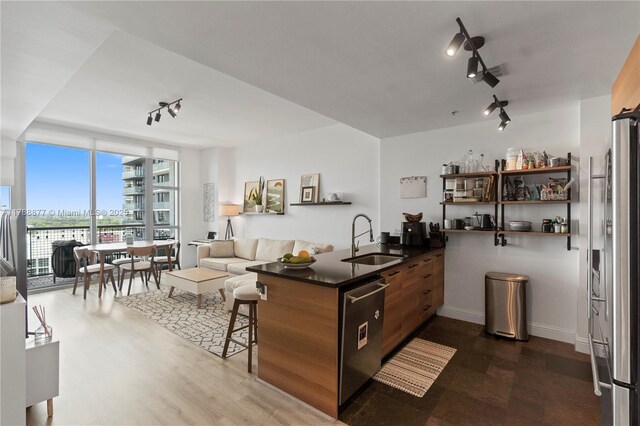 kitchen with dark countertops, a sink, rail lighting, and stainless steel appliances