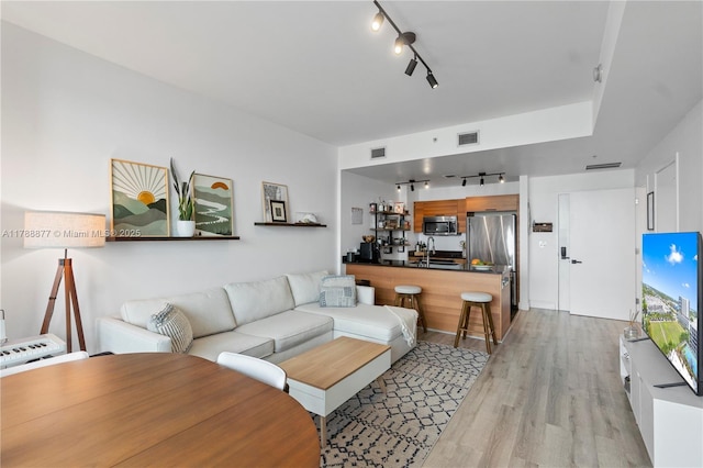 living area with rail lighting, visible vents, and light wood-style floors