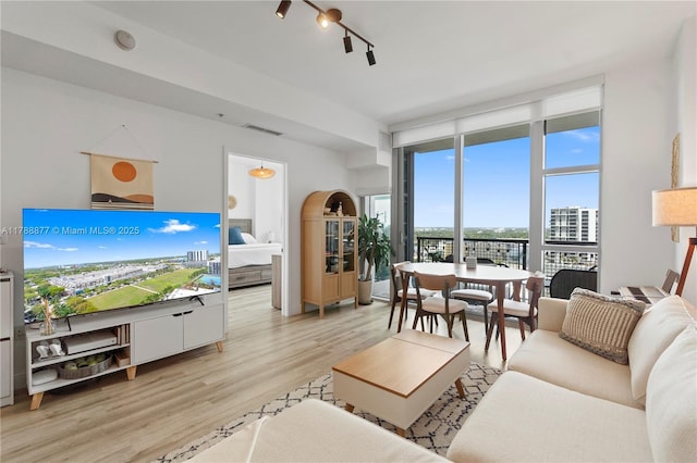living area featuring a view of city, visible vents, floor to ceiling windows, light wood-type flooring, and track lighting