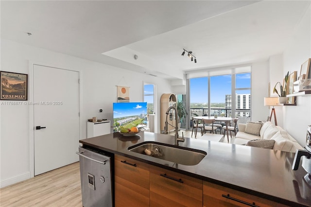 kitchen featuring a sink, light wood-style floors, stainless steel dishwasher, dark countertops, and open floor plan