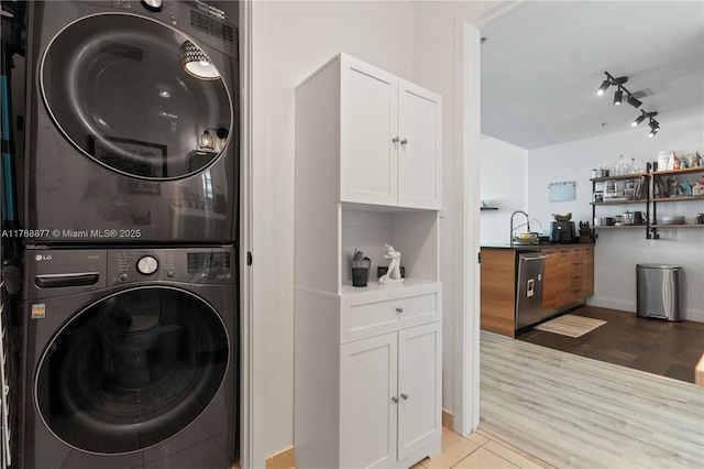 clothes washing area featuring a sink, stacked washing maching and dryer, rail lighting, laundry area, and wood finished floors