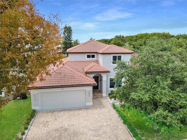 mediterranean / spanish-style home with stucco siding, driveway, a tiled roof, and an attached garage