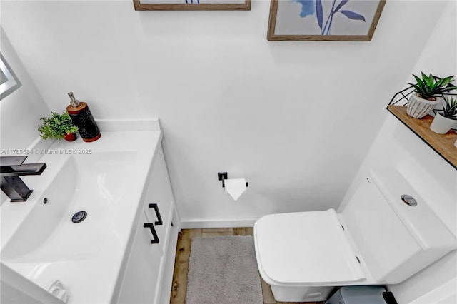 half bath with toilet, wood finished floors, and vanity