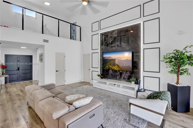 living area with a towering ceiling, a ceiling fan, wood finished floors, and baseboards