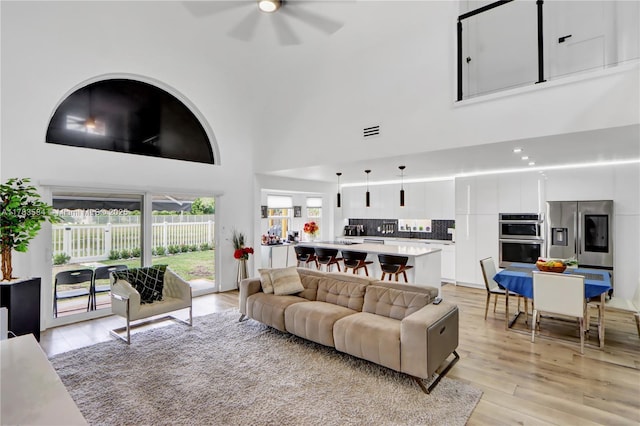 living room with visible vents, ceiling fan, light wood finished floors, and a high ceiling