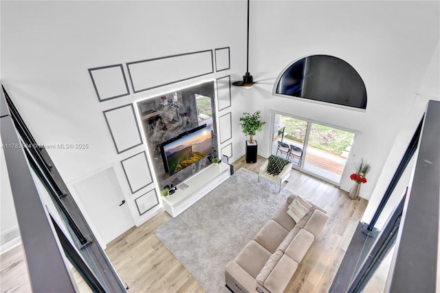 living room with ceiling fan, light wood-style flooring, and a high ceiling