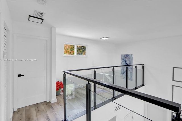 hallway featuring an upstairs landing, visible vents, and light wood-style flooring