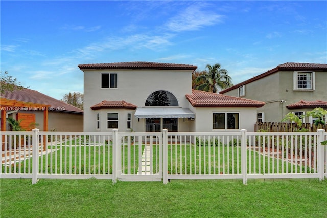 back of house featuring a tile roof, a lawn, a fenced front yard, and stucco siding