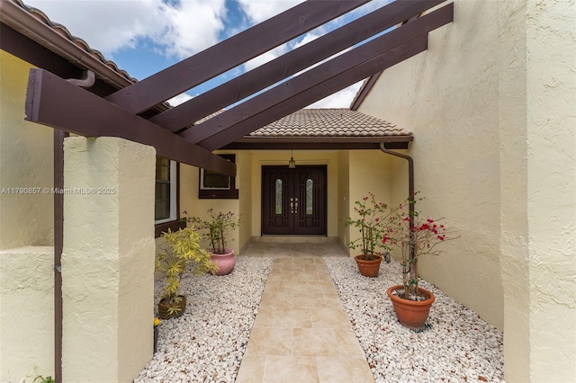 view of exterior entry featuring french doors, stucco siding, and a tiled roof
