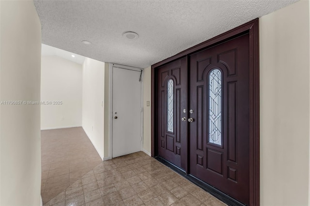 foyer entrance featuring a textured ceiling, baseboards, and light tile patterned flooring