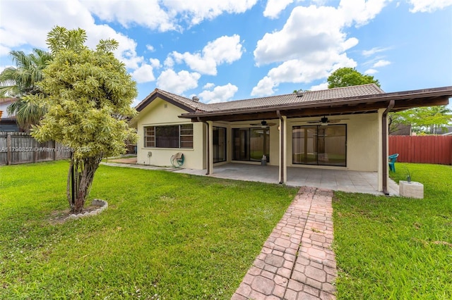 rear view of property featuring stucco siding, a yard, fence, a patio, and a ceiling fan