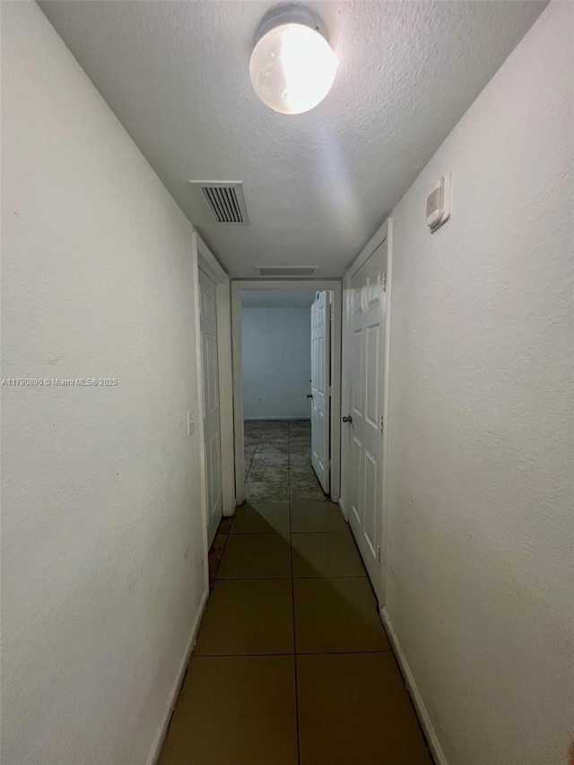 corridor featuring baseboards, visible vents, a textured ceiling, and tile patterned flooring