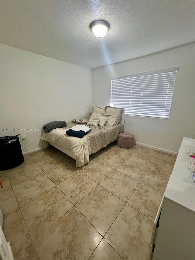 bedroom featuring a textured ceiling, light tile patterned floors, and baseboards