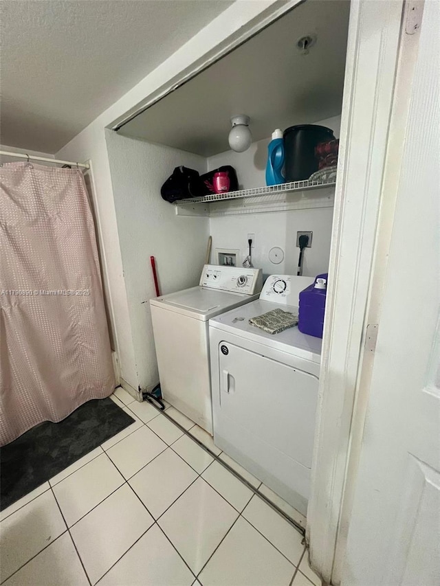 clothes washing area with light tile patterned flooring, independent washer and dryer, laundry area, and a textured ceiling