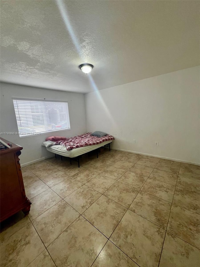 bedroom with baseboards, a textured ceiling, and light tile patterned flooring