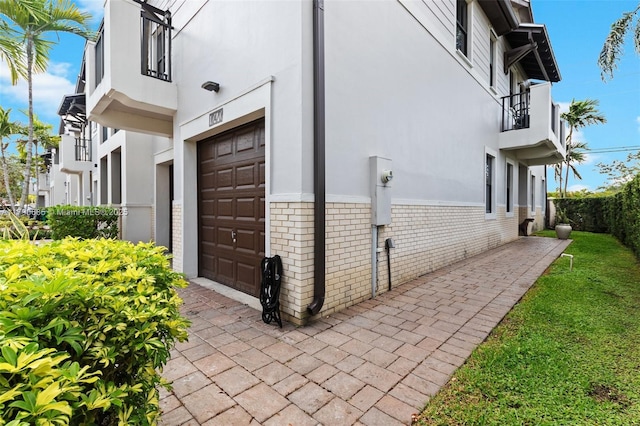 view of side of home with stucco siding, a balcony, brick siding, and a garage