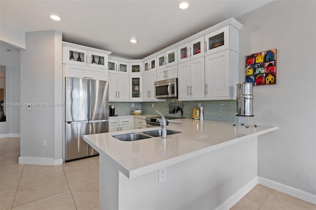 kitchen with tasteful backsplash, stainless steel appliances, light tile patterned floors, light countertops, and a peninsula