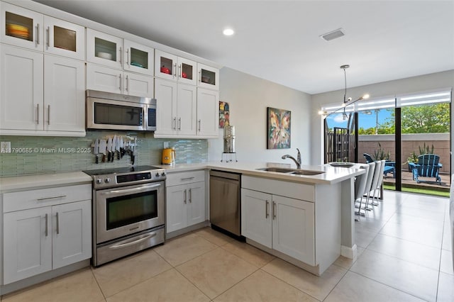 kitchen featuring a sink, stainless steel appliances, decorative backsplash, a peninsula, and light countertops