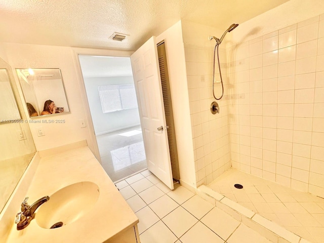 bathroom featuring tiled shower, a textured ceiling, tile patterned flooring, and vanity