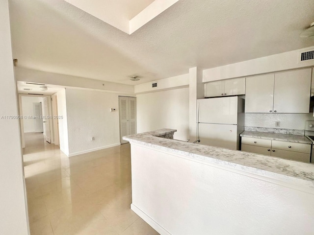 kitchen with light countertops, visible vents, baseboards, a textured ceiling, and freestanding refrigerator